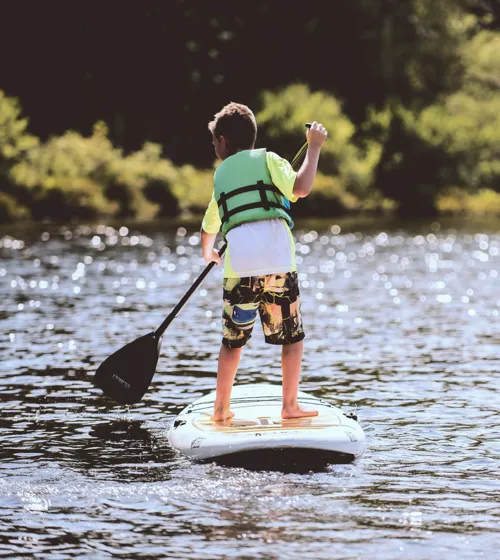 Un enfant debout sur une planche à pagaie sur un lac.