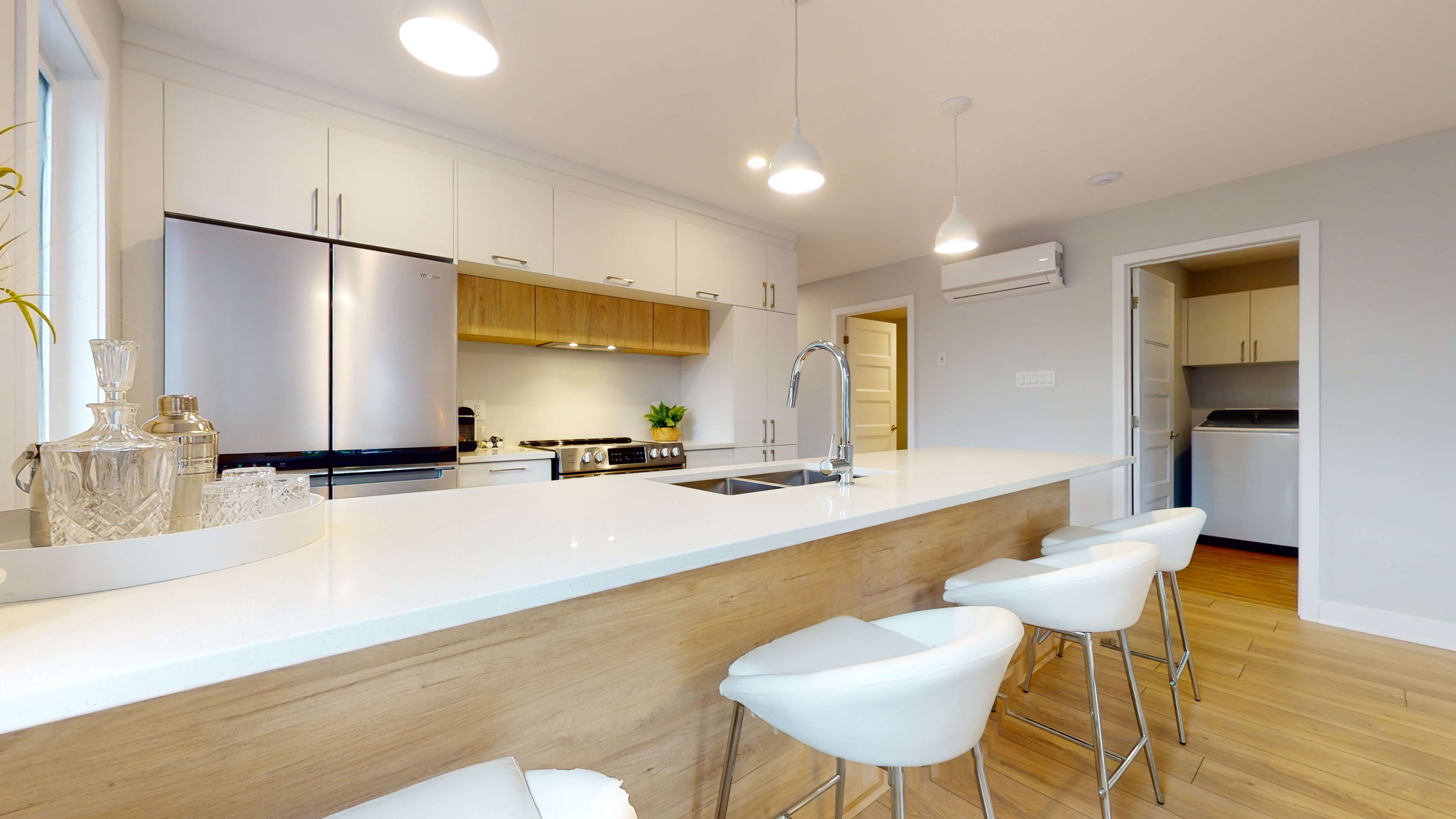 Une cuisine moderne et blanche de condo, avec des tabourets devant un ilot en avant plan.