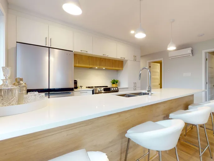 Une cuisine moderne et blanche de condo, avec des tabourets devant un ilot en avant plan.