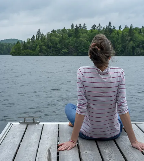 Femme assise sur un quai, face à un lac.